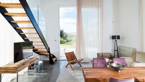 A modern living room with a wooden staircase, a TV, a dining table, and a sofa.