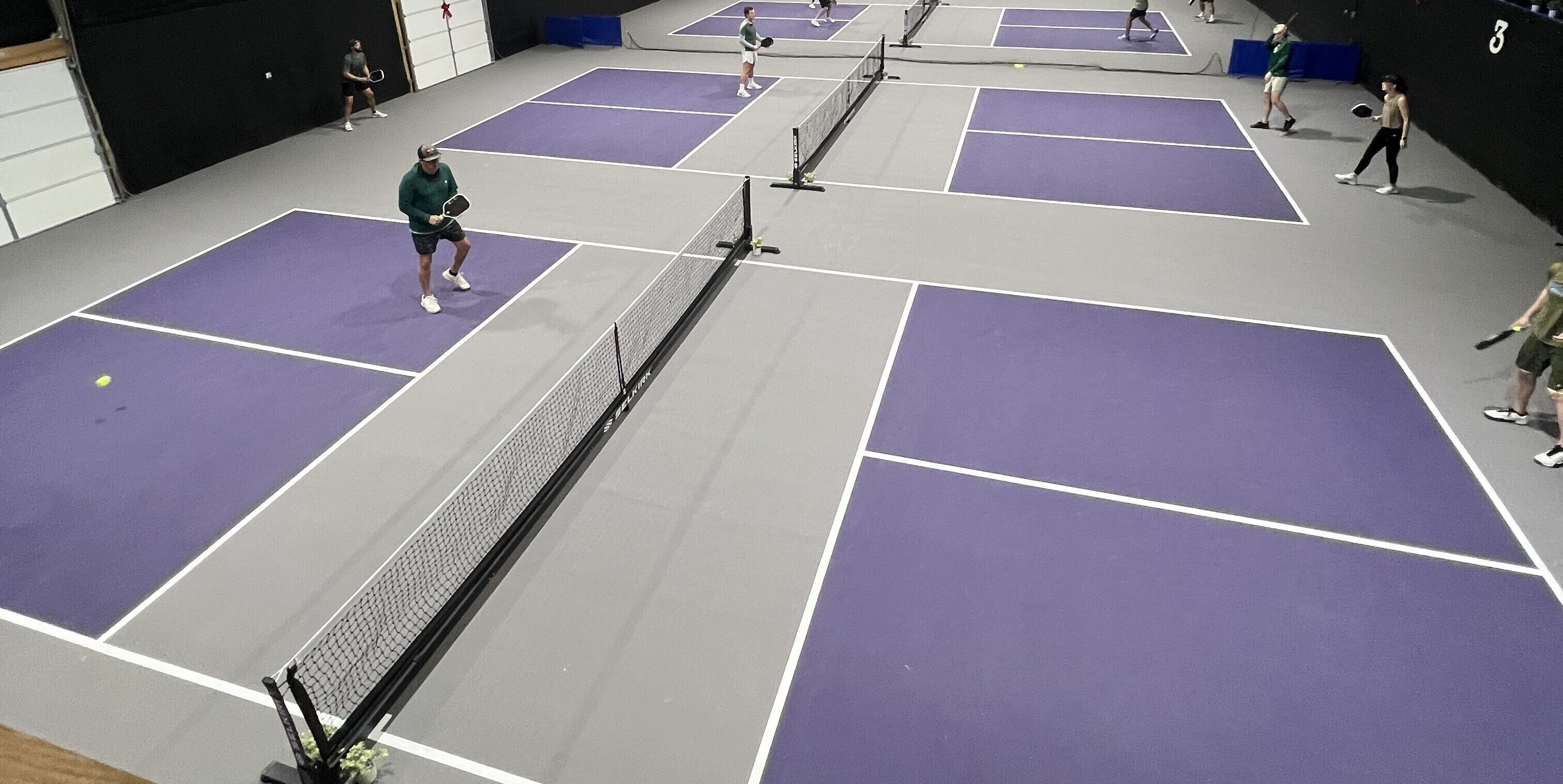 A multi-bench indoor tennis court with a net in the center.