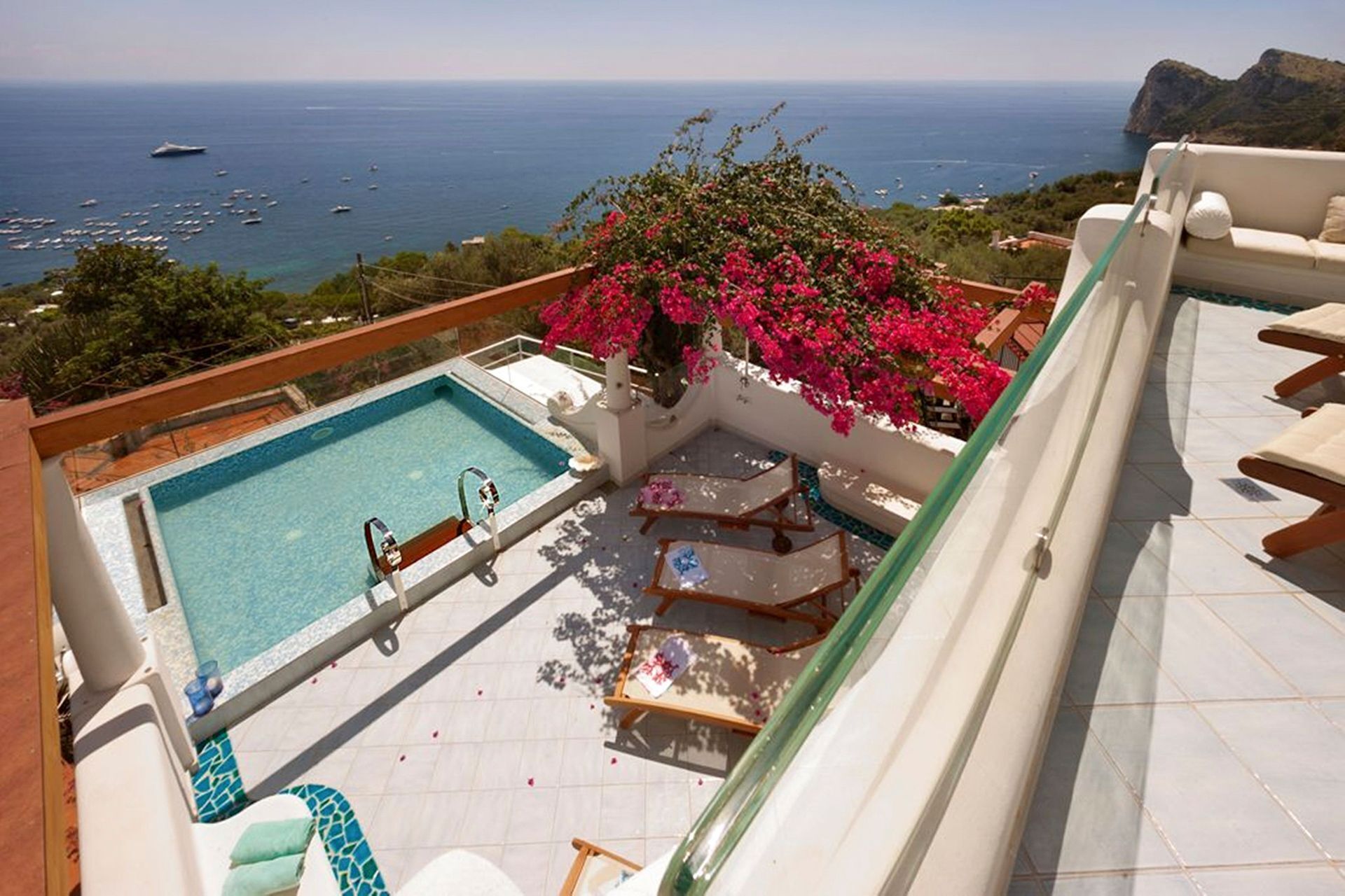 Una piscina sul tetto con vista sul mare, circondata da lettini e un muro ricoperto di fiori.