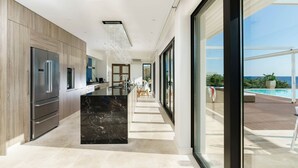 A modern kitchen with a marble island, stainless steel appliances, and a view of a pool and ocean. - Villa Incanto - Four Bedroom Villa, Sleeps 8 (Plemmirio)