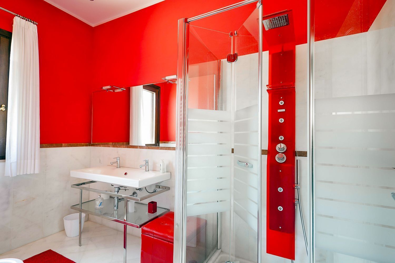 A modern bathroom with a glass shower enclosure, a white sink, and a red accent wall.