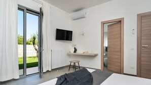 Ein modernes Schlafzimmer mit einem großen Bett, einem an der Wand montierten Fernseher, einem kleinen Hocker und einer Schiebetür, die auf einen Balkon führt.