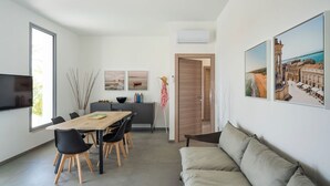 Ein modernes Wohnzimmer mit einer Couch, einem Esstisch mit Stühlen, einem Fernseher und Kunstwerken an den Wänden.