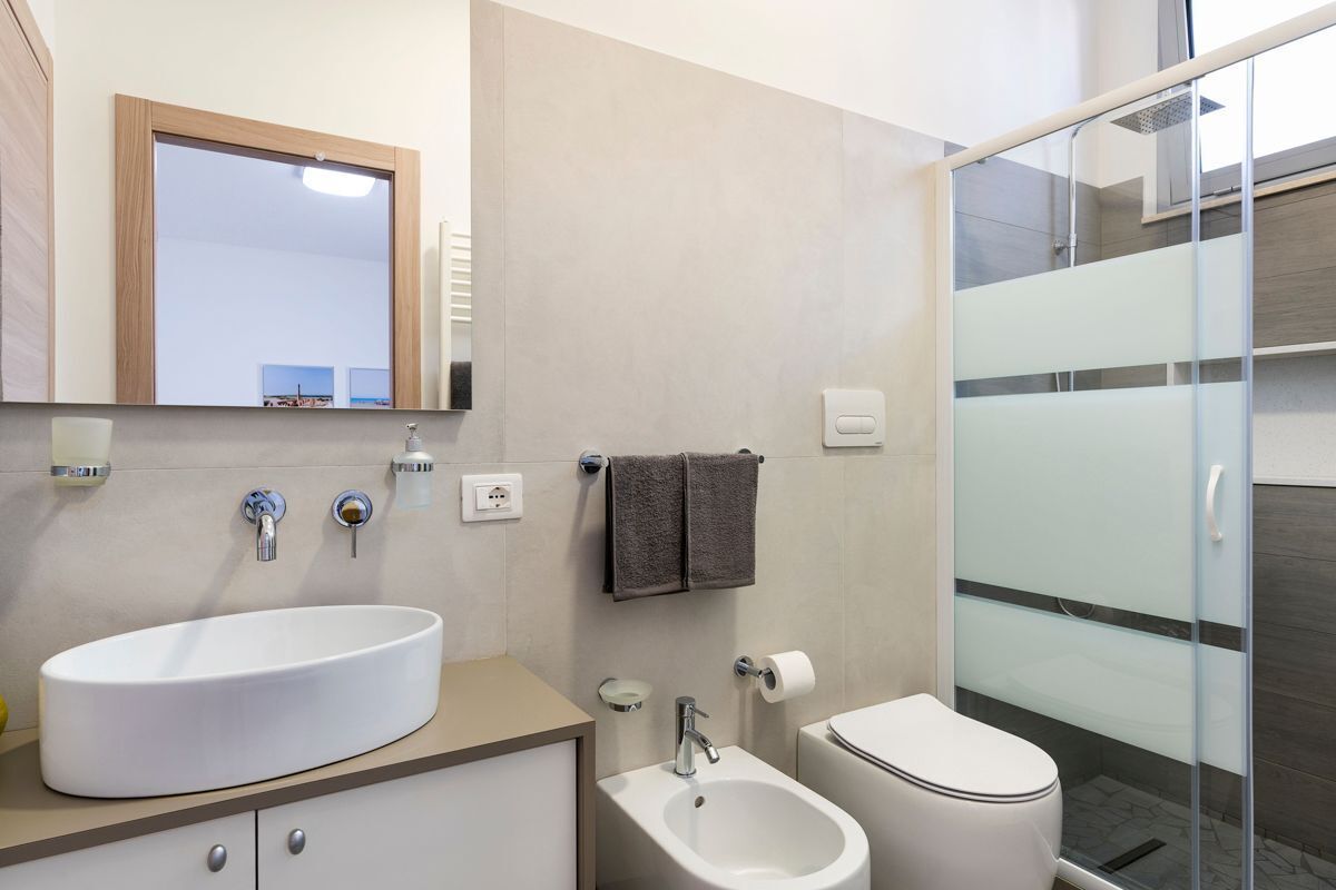 Een moderne badkamer met een groot ovaal wastafel, een bidet, toilet en een douchecabine van glas.