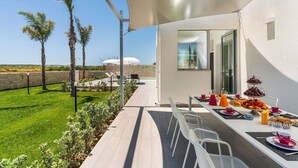 Ein moderner Essbereich im Freien mit einer Terrasse, Palmen und Blick auf das Meer.