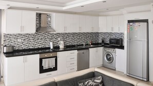 A modern kitchen with white cabinets, a black countertop, a tiled backsplash, a built-in oven, a dishwasher, a washing machine, and a refrigerator. - Villa Gunes - Three Bedroom Villa, Sleeps 6 (Ölüdeniz Belediyesi)
