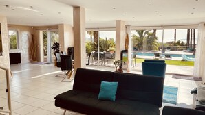A modern living room with a black sofa, a dining area with chairs and a table, and a view of a pool and outdoor area. - Villa 6pers splendid sea view and magnificent landscaped park in the peace with swimming pool (Grosseto-Prugna)