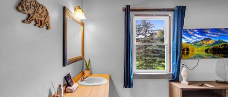 Un baño moderno con tocador de madera, espejo, lavamanos y ventana con vistas a un paisaje montañoso.
