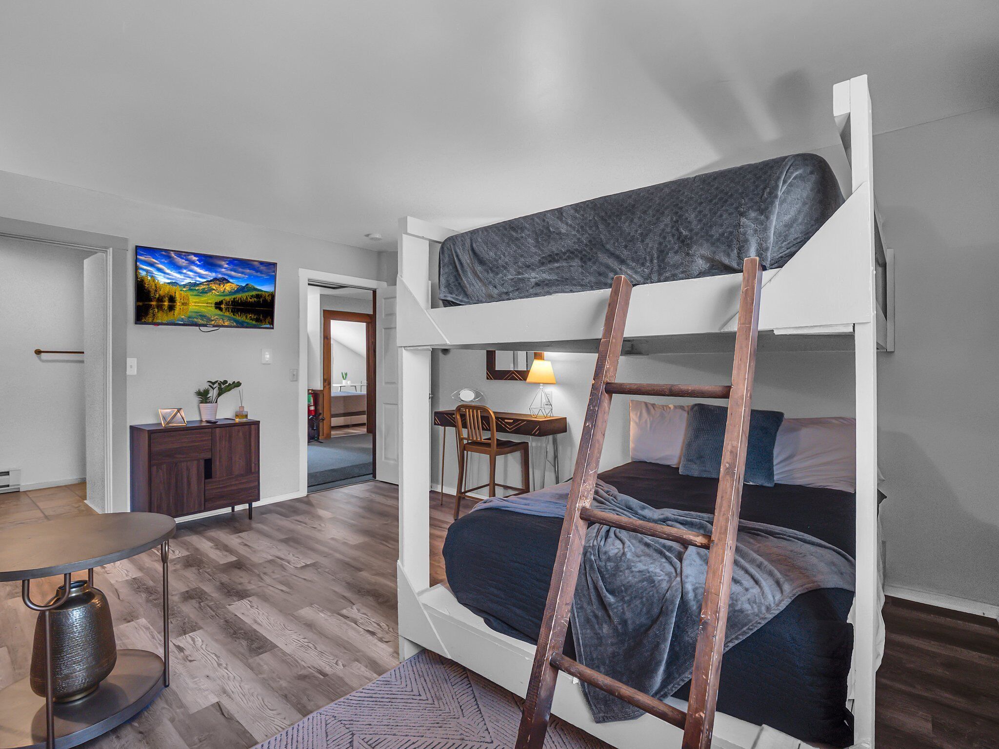 Una cama litera con escalera, un escritorio con silla, un televisor en la pared y piso de madera.
