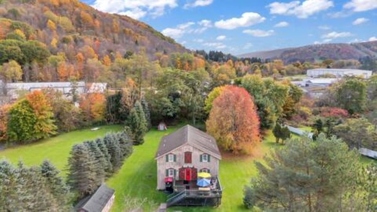 A two-story house with a red door, surrounded by a well-maintained lawn and trees with autumn foliage.