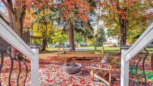 A covered outdoor seating area with a fire pit, surrounded by trees with autumn leaves. - Timberline Lodge (Ellicottville)