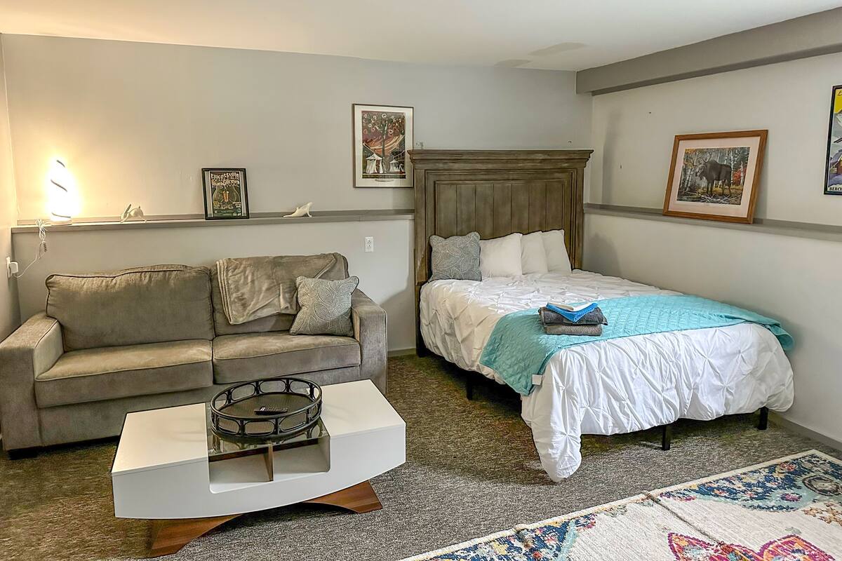 A bedroom with a bed, a sofa, a coffee table, and a carpeted floor.
