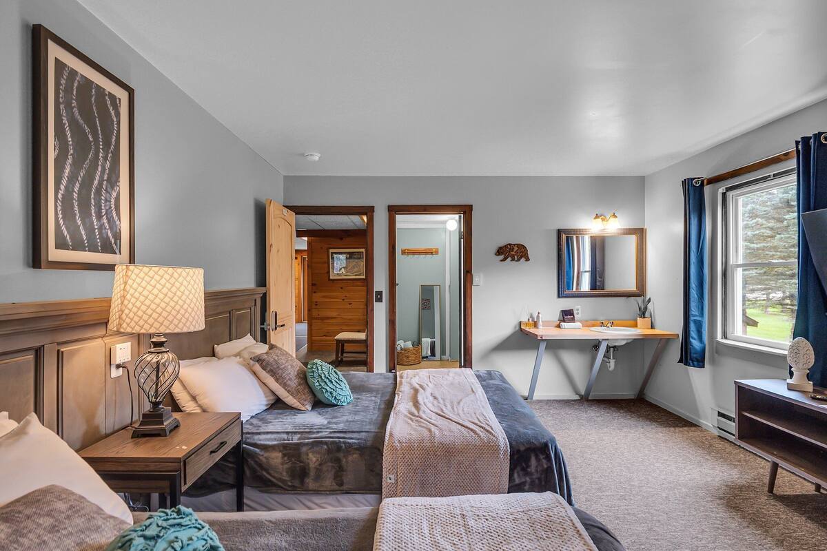 A hotel room with two beds, a desk, a mirror, and a window with curtains.