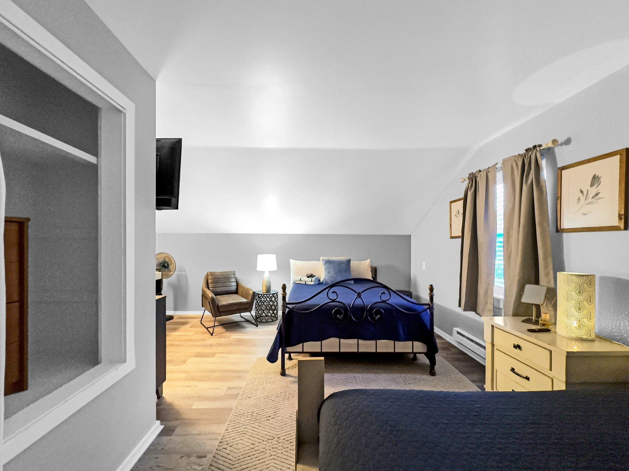 Ein Schlafzimmer mit einem Bett, einem Sessel, einem Nachttisch, einer Lampe und einem an der Wand montierten Fernseher.