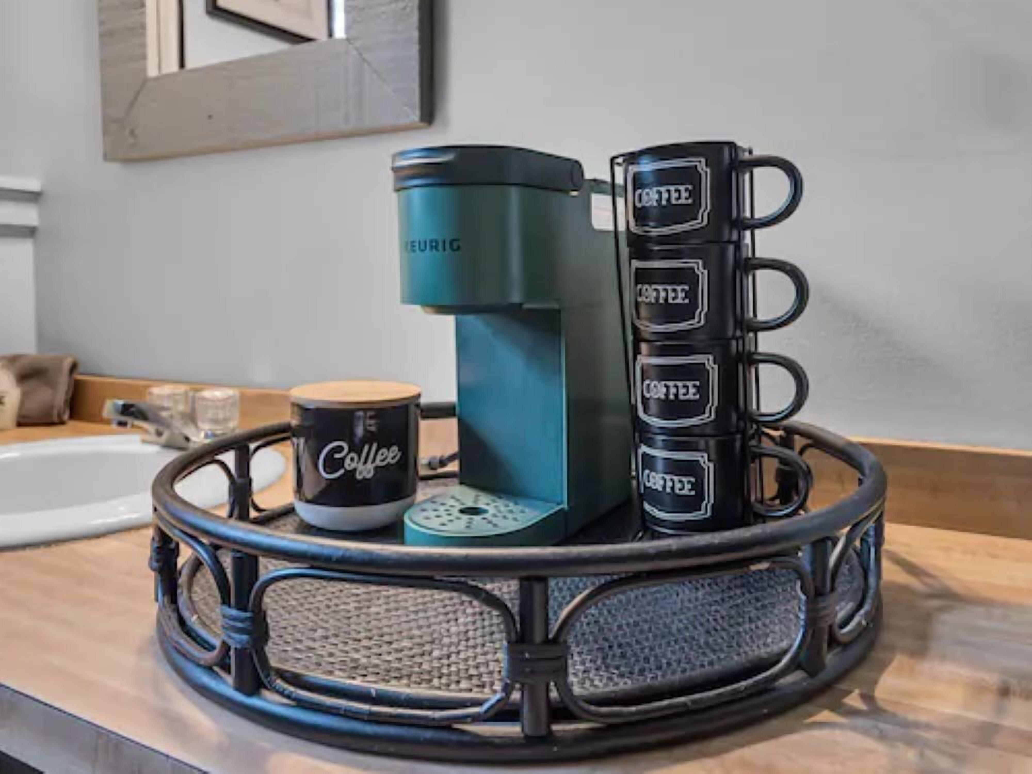 Een koffiezetapparaat, een koffiemok en een dienblad met meerdere koffiemokken op een aanrecht.