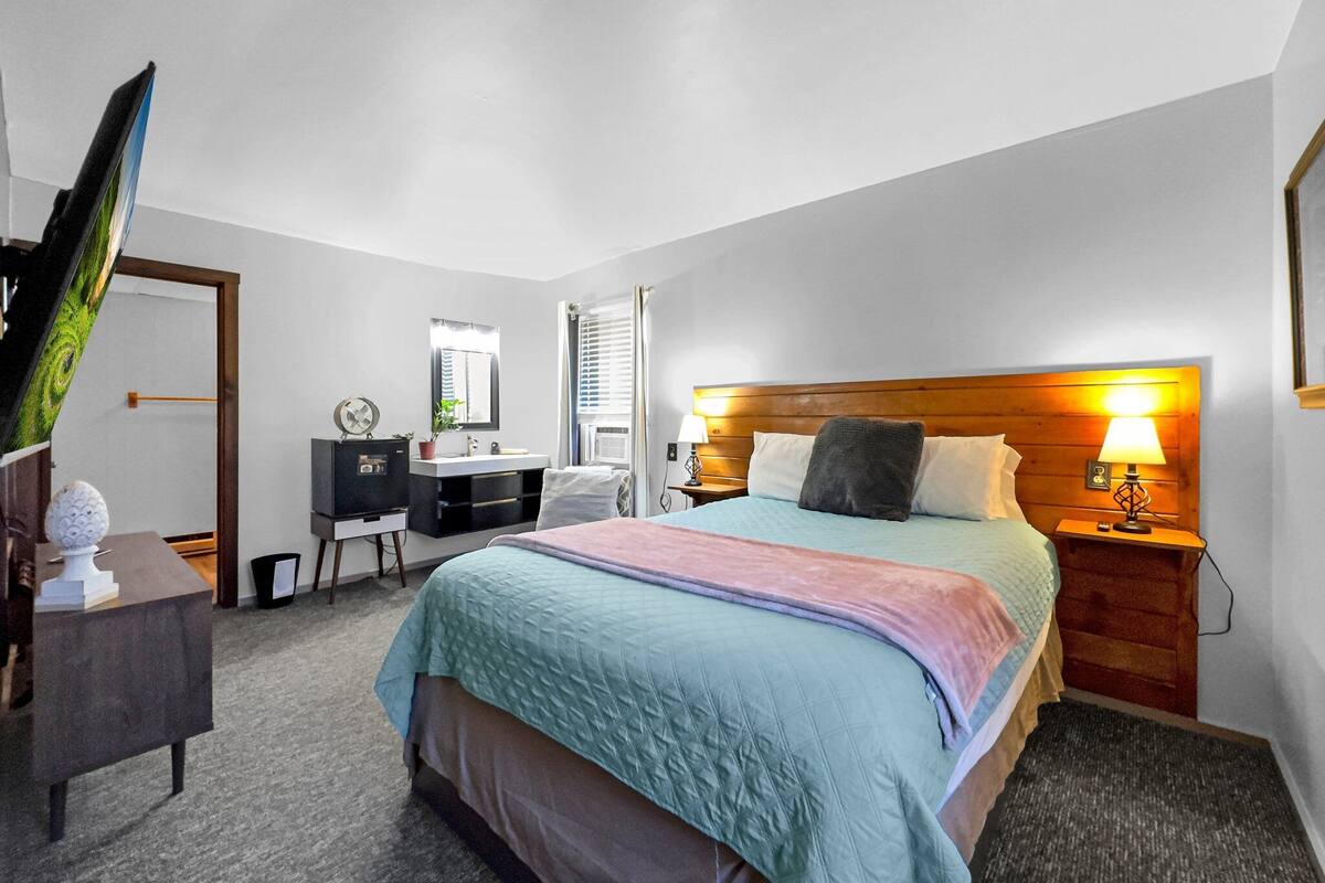 A bedroom with a bed, bedside tables, a dresser, a mirror, and a window.