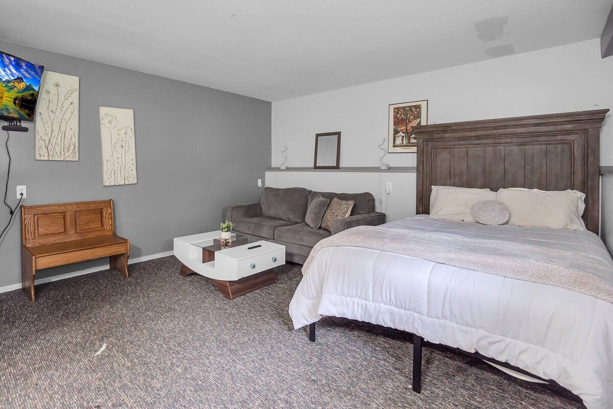 A bedroom with a bed, a sofa, a small table, and a bench.