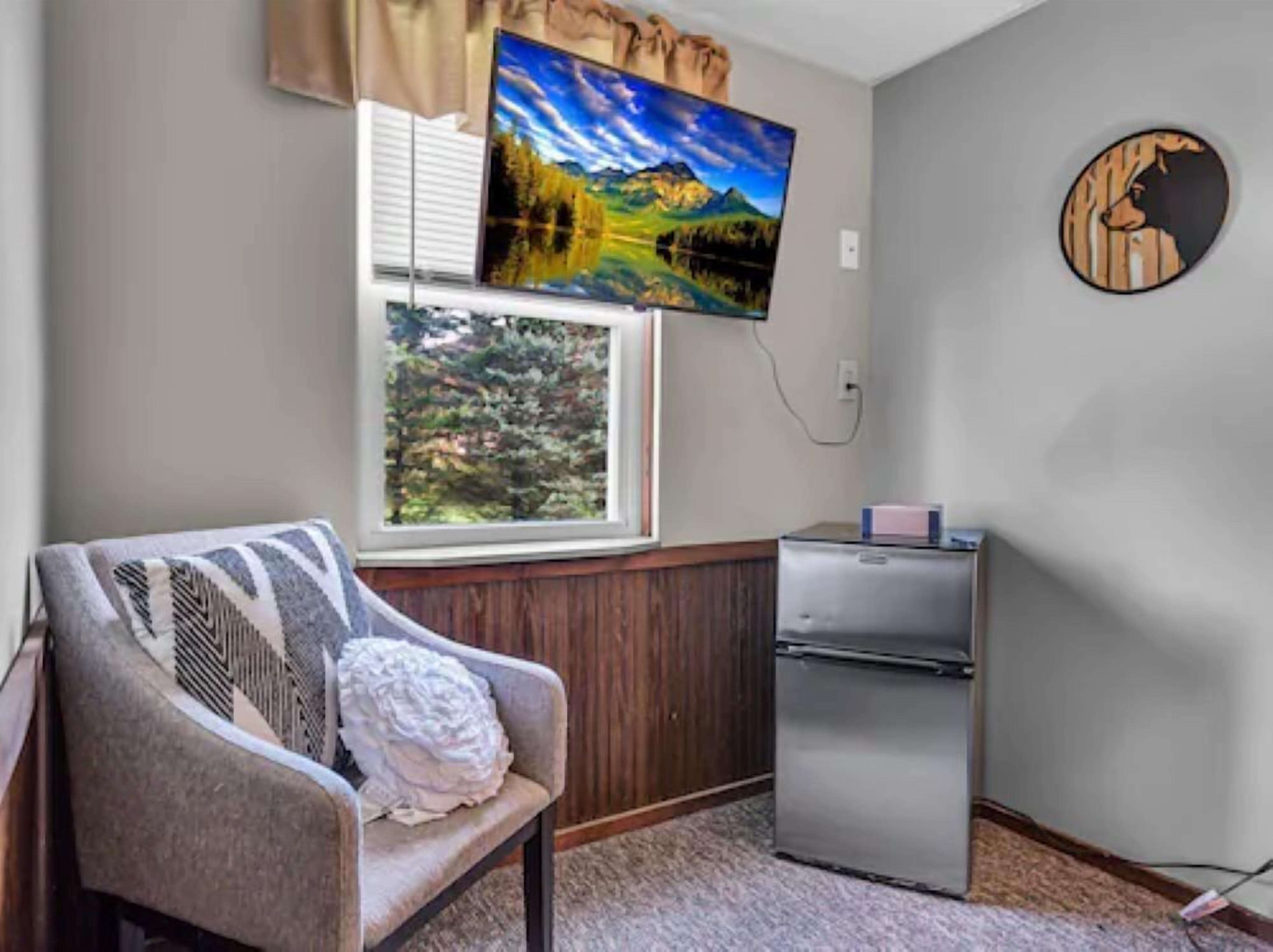A room with a bed, a window, a TV mounted on the wall, and a small refrigerator.