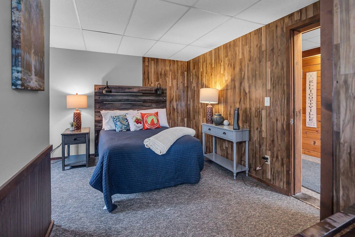 A bedroom with a wooden headboard, a bed with a blue quilt, two bedside tables with lamps, and a door with a sign.