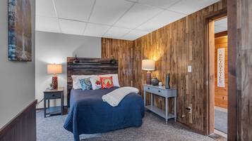 Un dormitorio con cabecera de madera, una cama con colcha azul, dos mesitas de noche con lámparas y una puerta con un cartel.