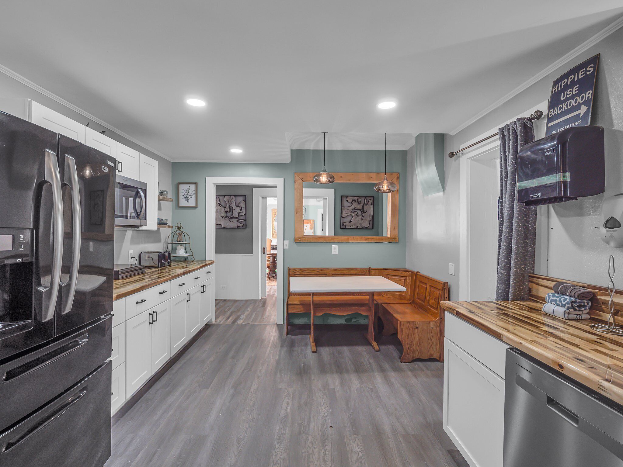 Una cocina moderna con refrigerador, microondas y lavavajillas incorporados. Hay una mesa de madera con bancos y una lámpara colgante arriba.