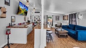 A spacious living area with a blue sofa, wooden flooring, and a kitchen area with a bar. - Timberline Lodge (Ellicottville)