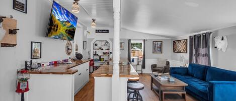 A spacious living area with a blue sofa, wooden flooring, and a kitchen area with a bar.
