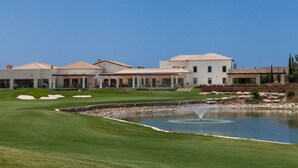Um campo de golfe com lago, clube e edifícios residenciais.
