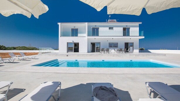 A modern two-story building with a swimming pool, white exterior, and multiple lounge chairs. - Villa Jason - Six Bedroom Villa, Sleeps 12 (Paralimni)