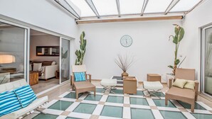 Une terrasse ensoleillée avec un sol à carreaux, des meubles en osier et des plantes en pot.