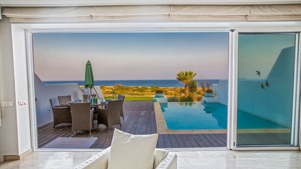 Un salon moderne avec une porte vitrée donnant sur une piscine et offrant une vue sur l’océan.