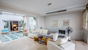 Un salon moderne avec un canapé, une table basse et un téléviseur. Une porte-fenêtre coulissante donne accès à un balcon.
