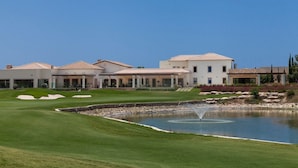 A golf course with a pond, a clubhouse, and residential buildings.