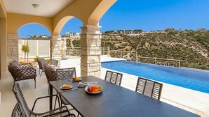 A terrace with a pool, outdoor seating, and a view of a hillside.