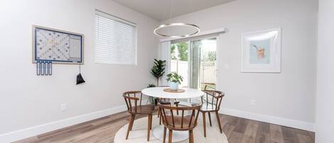 Een eethoek met een ronde tafel, zes houten stoelen, een wit vloerkleed en een hanglamp.