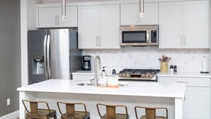 A modern kitchen with white cabinets, stainless steel appliances, and a central island with bar stools. - Fun & Good Vibes in Meridian (Meridian)