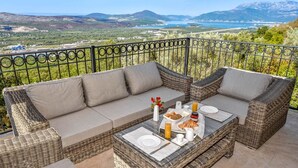 A wicker sofa set with a breakfast table, a vase with flowers, and a scenic view of mountains and a lake. - Villa Kotop - Three Bedroom Villa, Sleeps 6 (Dub, Kotor)