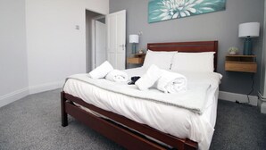 A neatly made bed with white linens and towels, a wooden headboard, and a wall-mounted painting of a flower. - Modern 2 Bedroom Flat in Robert st, Swansea (Swansea)