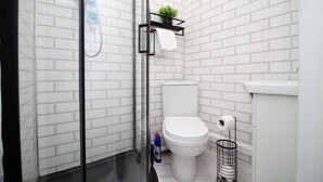 A modern bathroom with white subway tiles, a glass shower enclosure, a toilet, and a small shelf with a plant. - Modern 2 Bedroom Flat in Robert st, Swansea (Swansea)