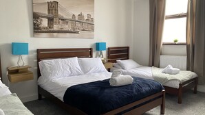 A hotel room with a large bed, two bedside tables, a nightstand, a window with curtains, and a cityscape painting on the wall. - Modern 2 Bedroom Flat in Robert st, Swansea (Swansea)