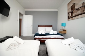 A hotel room with a bed, two bedside tables, a TV, and a painting on the wall.