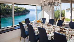 Un comedor con vistas al mar, un candelabro y una mesa dispuesta con platos y copas.