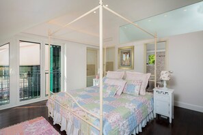 Une chambre à coucher avec un lit à baldaquin, une table de chevet, un miroir et une vue sur le balcon extérieur.