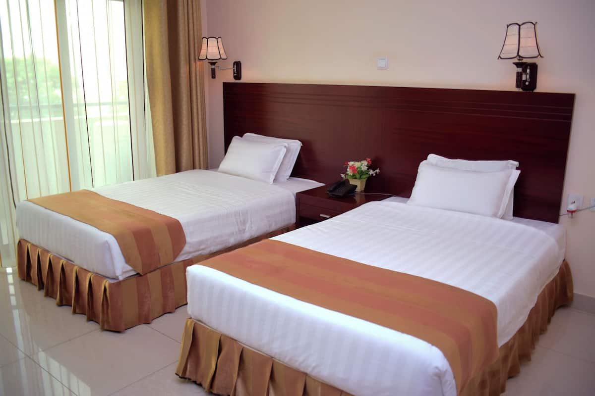 Two single beds with matching headboards and footboards, a nightstand with a phone and a vase of flowers, and a window with curtains.