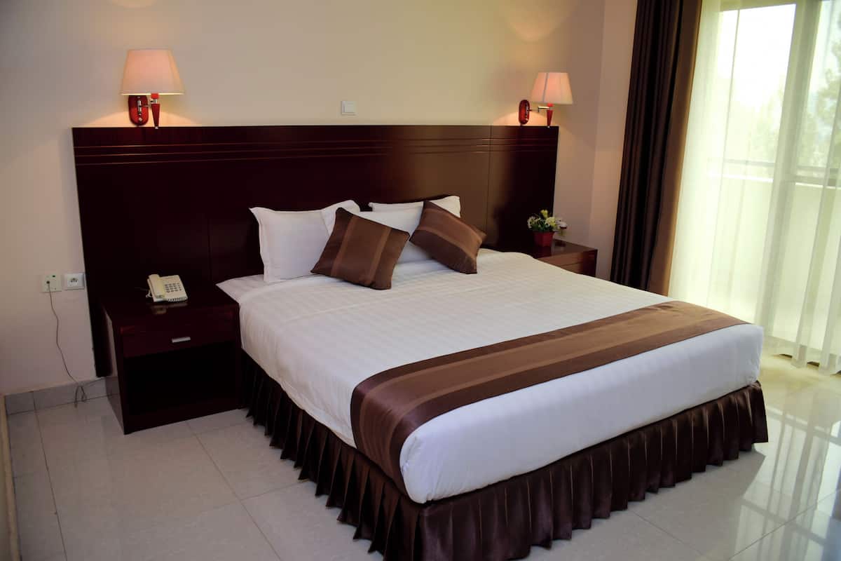 A hotel room with a large bed, two bedside tables with lamps, a telephone, and a window with curtains.