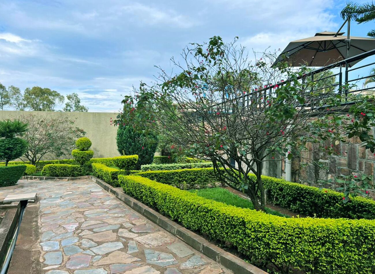 A stone pathway leading through a well-manicured garden with neatly trimmed hedges and a variety of trees.