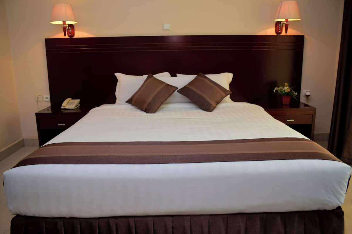 A neatly made bed with a dark headboard, two bedside lamps, a telephone, and a small table with a flower vase.