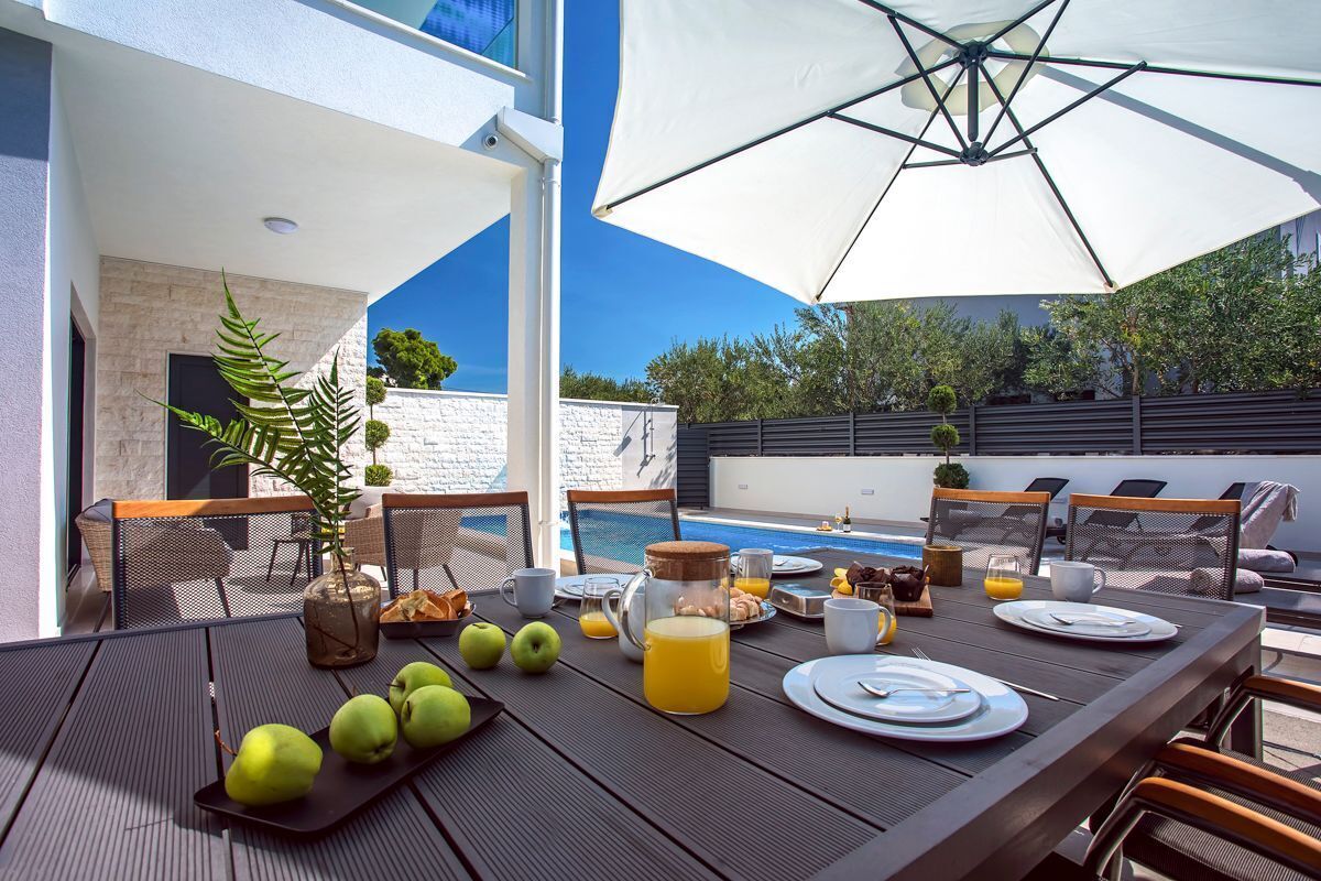 Un espace extérieur aménagé pour les repas, avec une piscine, une table à manger, des chaises et des parasols.