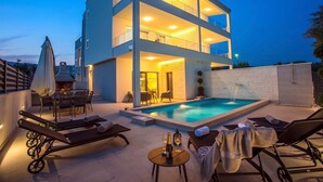 A modern two-story building with a rooftop pool, lounge chairs, and a dining area.