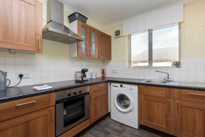 Una cocina con armarios de madera, estufa de acero inoxidable, horno empotrado, lavadora y ventana con vistas.